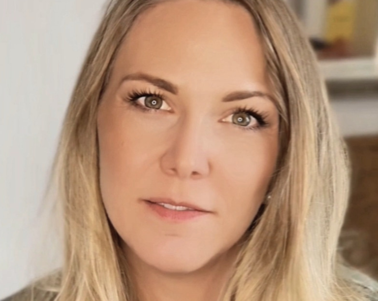 Porträt einer Frau mit langen, blonden Haaren und einem neutralen Ausdruck.